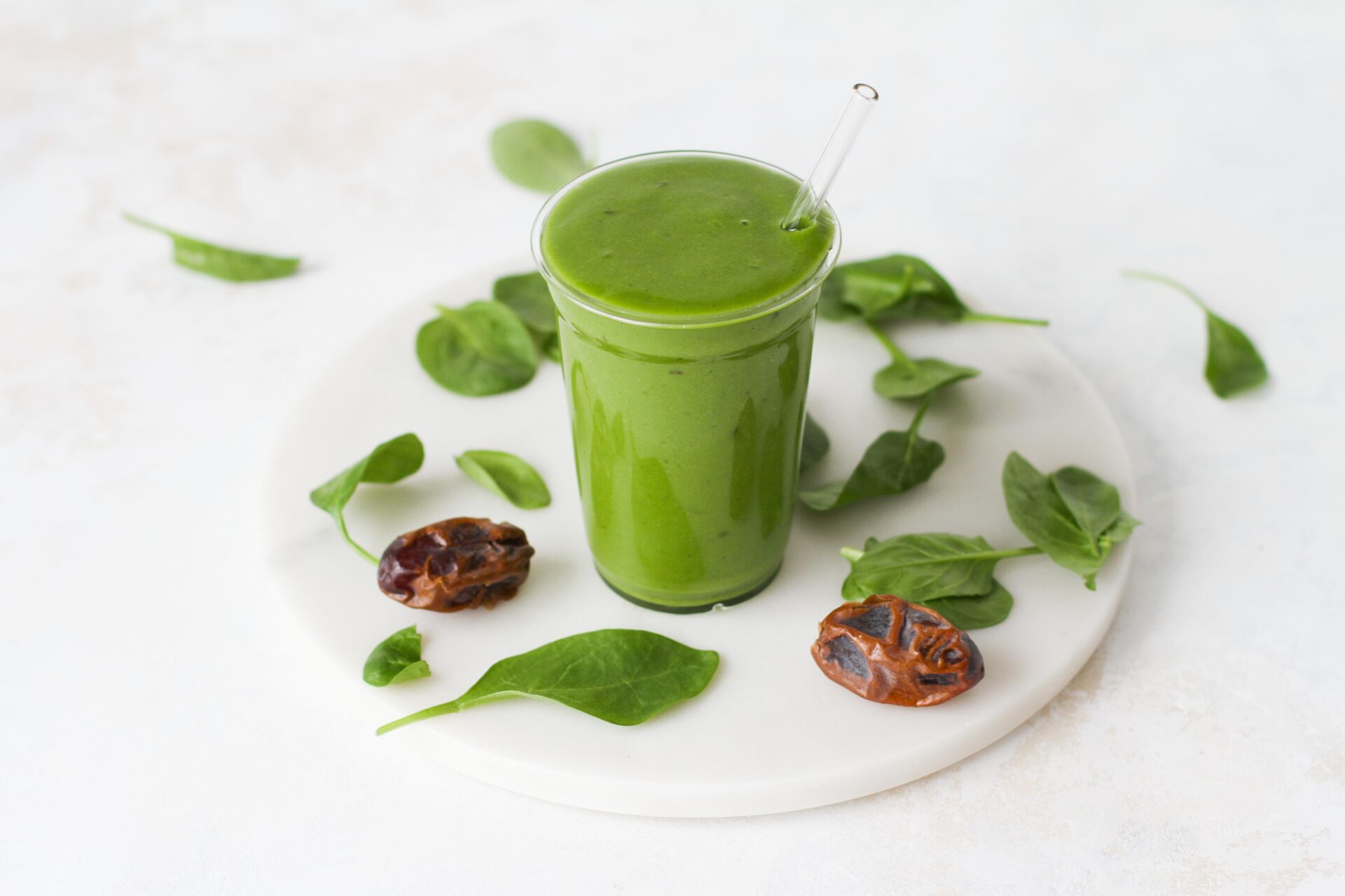 A vibrant green mango spinach smoothie in a glass garnished with fresh spinach and dates.