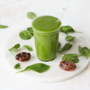 A vibrant green mango spinach smoothie in a glass garnished with fresh spinach and dates.